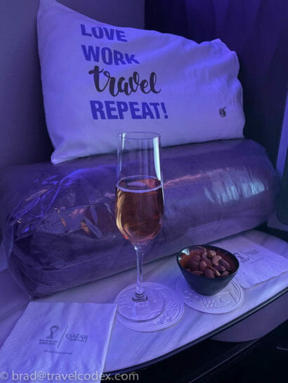 a glass of wine and a bowl of nuts on a bed