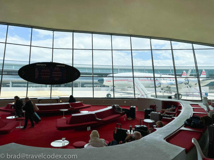 a group of people in a lounge area with red seats and airplanes in the background