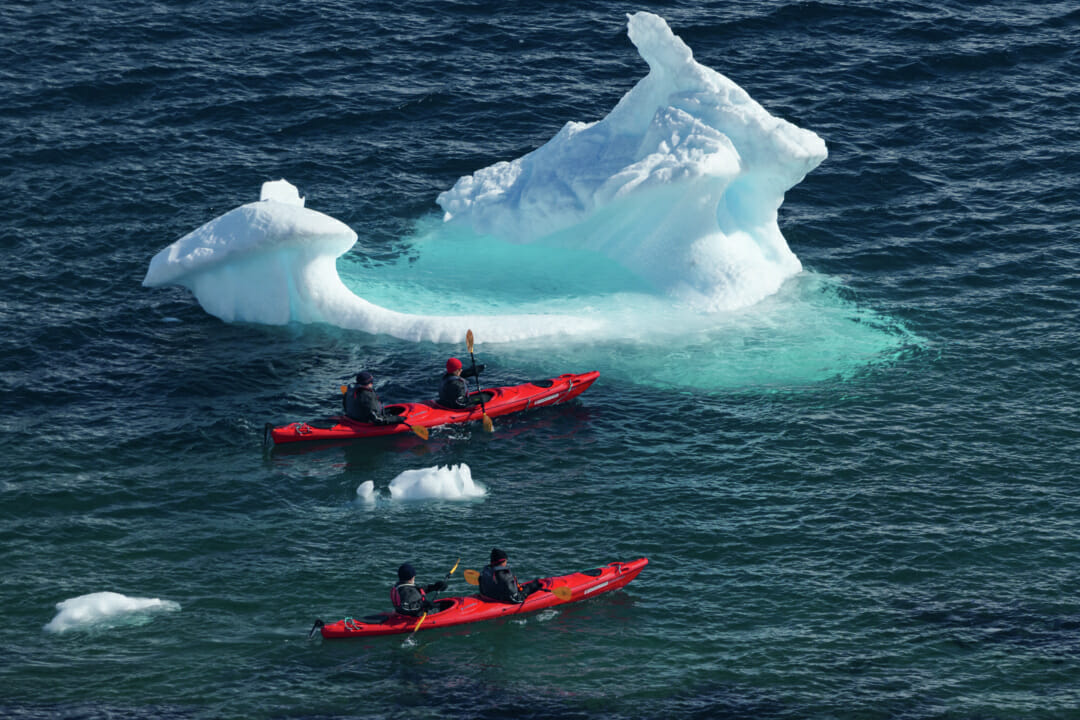 people kayaks in the water with an iceberg in the background