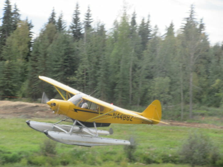 a yellow plane flying over grass