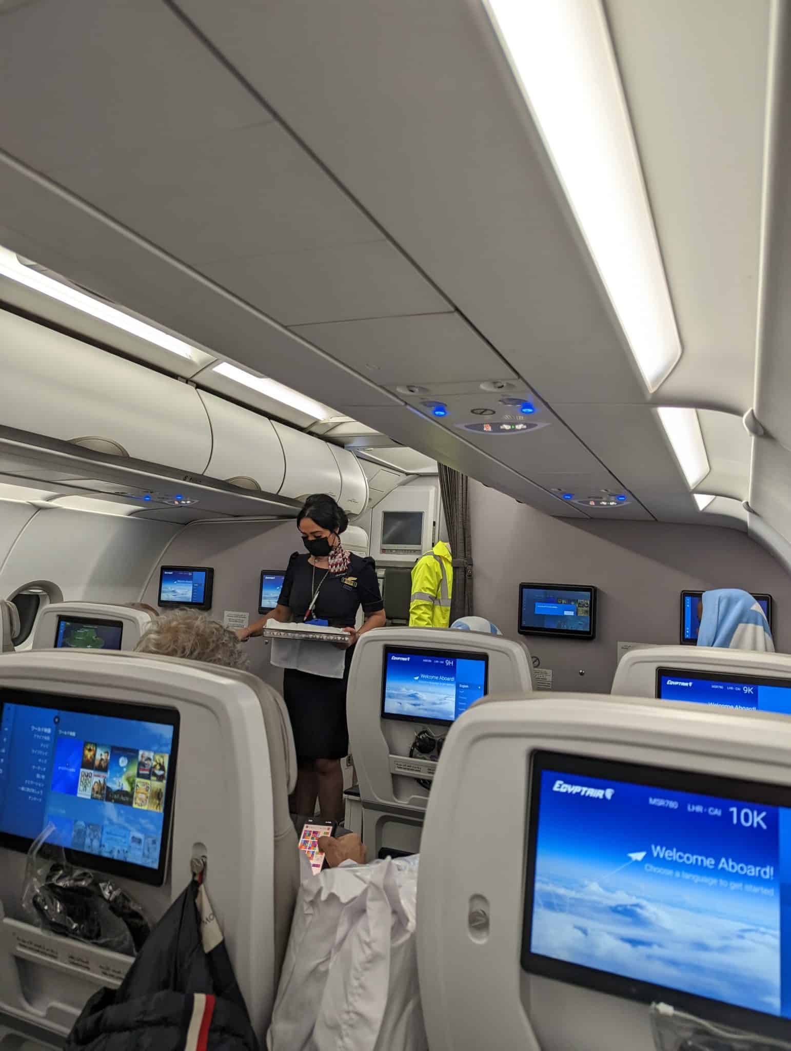 a woman in a mask standing in an airplane with several monitors
