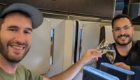 two men sitting in a plane with glasses of wine