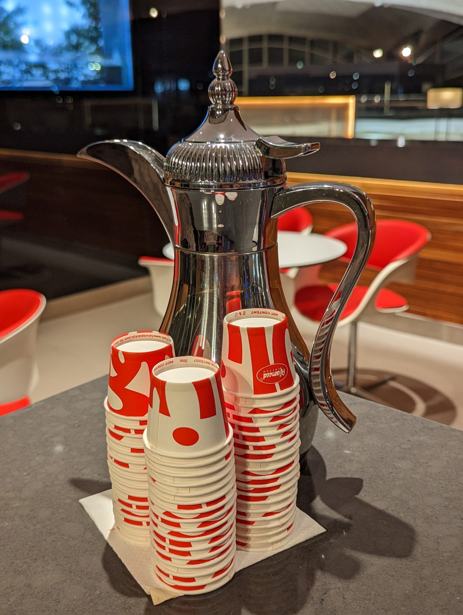 a silver coffee pot and stack of paper cups
