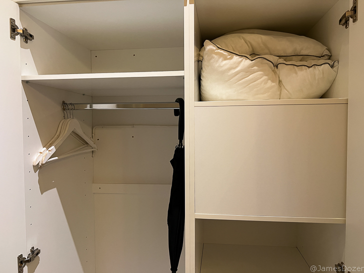 a closet with a white shelf and a black umbrella