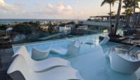 a pool with white chairs and trees and a building with a body of water