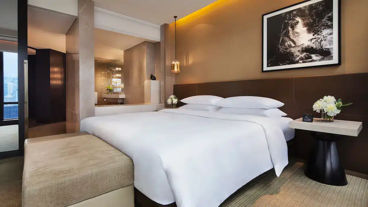 a bed with white sheets and a bench in a hotel room