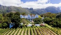 a large white house with a large garden and mountains in the background