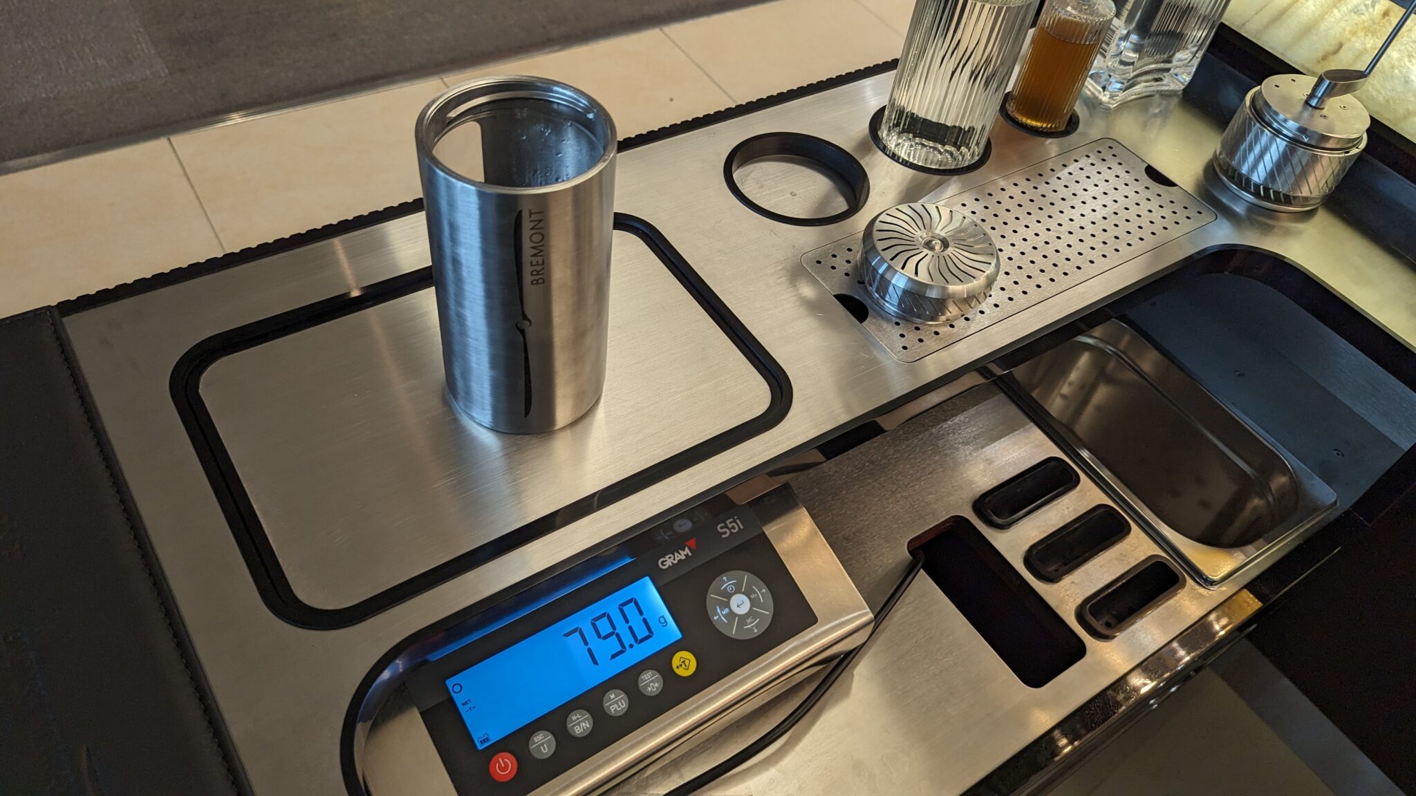 a scale with a silver cylinder and a glass of liquid on it