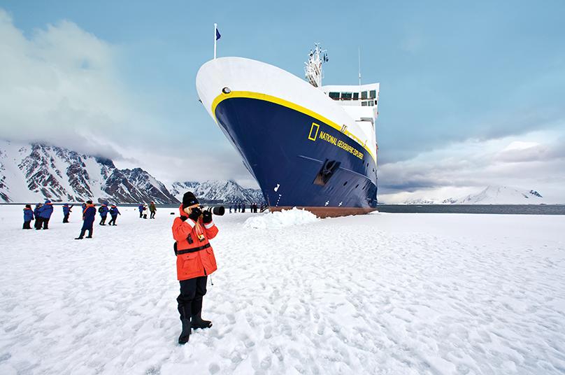 a person in a red jacket standing in the snow next to a large ship