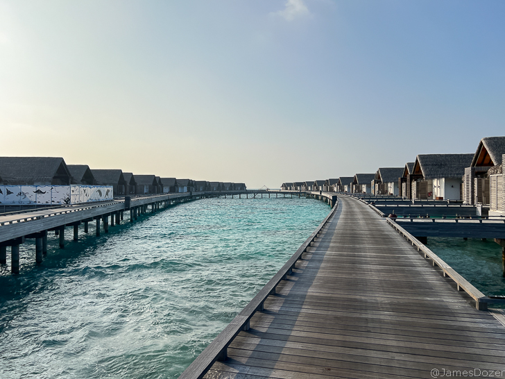 a long wooden walkway leading to a body of water with houses on the side