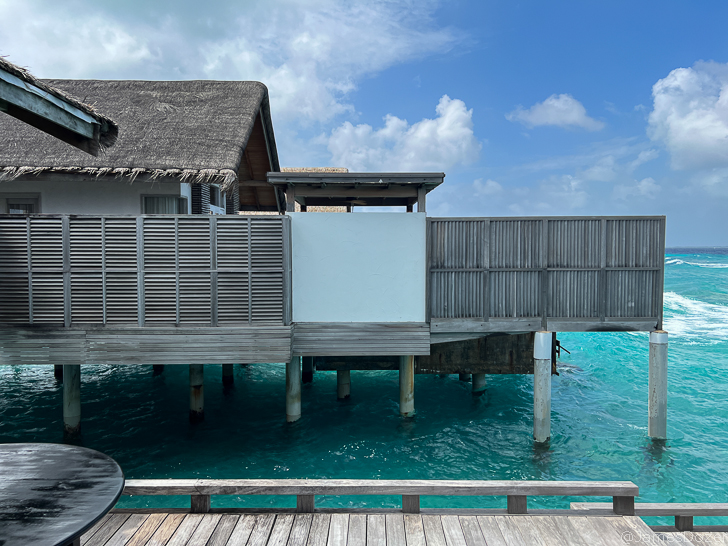 a wooden deck over water with a building and a thatched roof