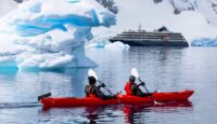 two people in a kayak in the water with a cruise ship in the background
