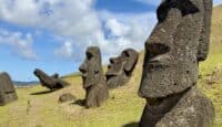 a group of stone statues on a hill with Easter Island in the background