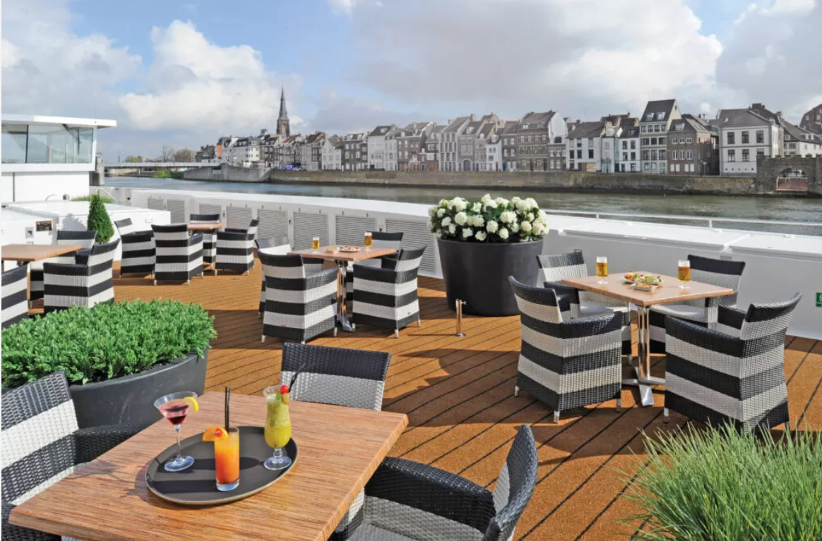 a restaurant on a deck with a river and buildings in the background