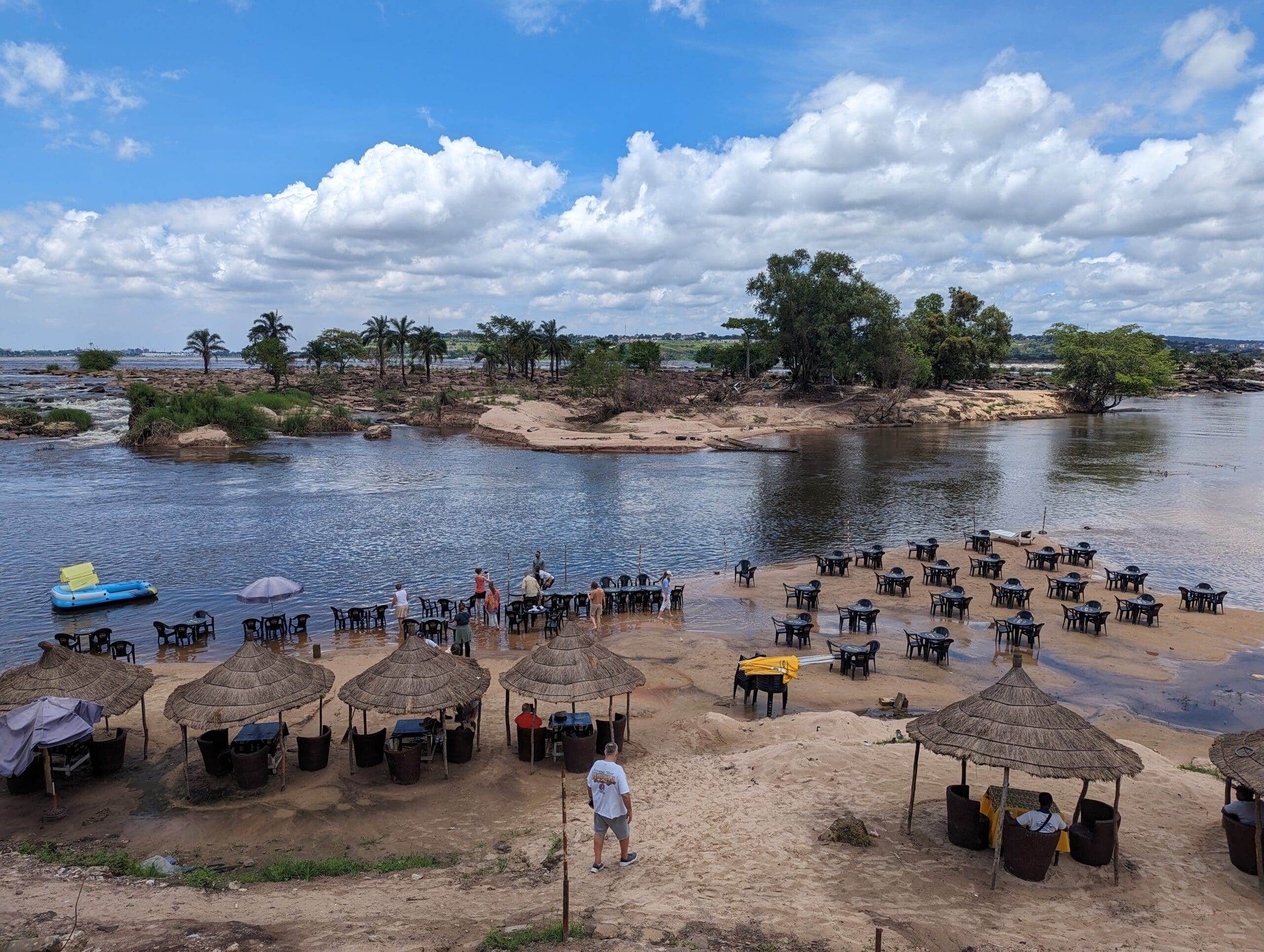 a group of people standing on a beach with tables and umbrellas